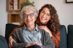 Happy young woman with eyeglasses hugging from behind older grandma with spectacles